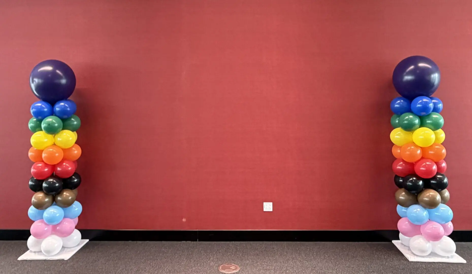Two colorful balloon columns against red wall